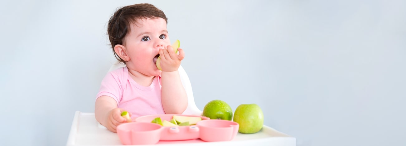 Niña llevando una rebanada de fruta a su boca con sus manos.