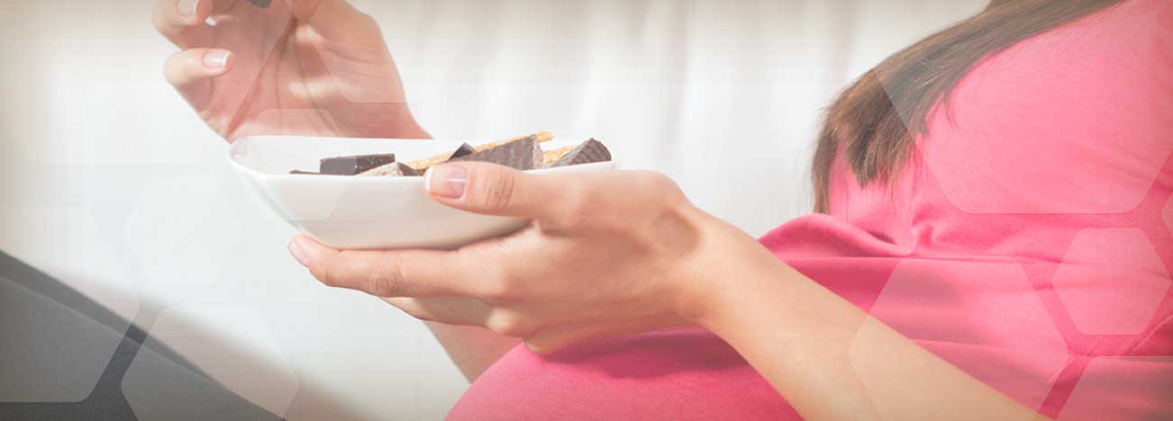 Mujer embarazada sosteniendo con sus manos un plato y una galleta de chocolate.