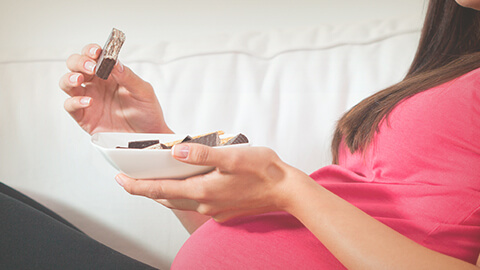 Mujer embarazada sosteniendo con sus manos un plato y una galleta de chocolate.