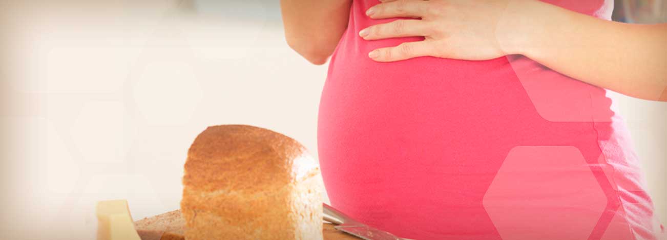 Mujer embarazada sosteniendo un sándwich mientras toca su vientre.