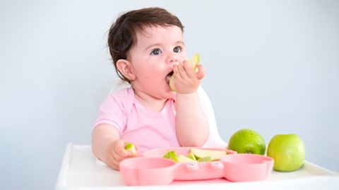 Niña llevando una rebanada de fruta a su boca con sus manos.