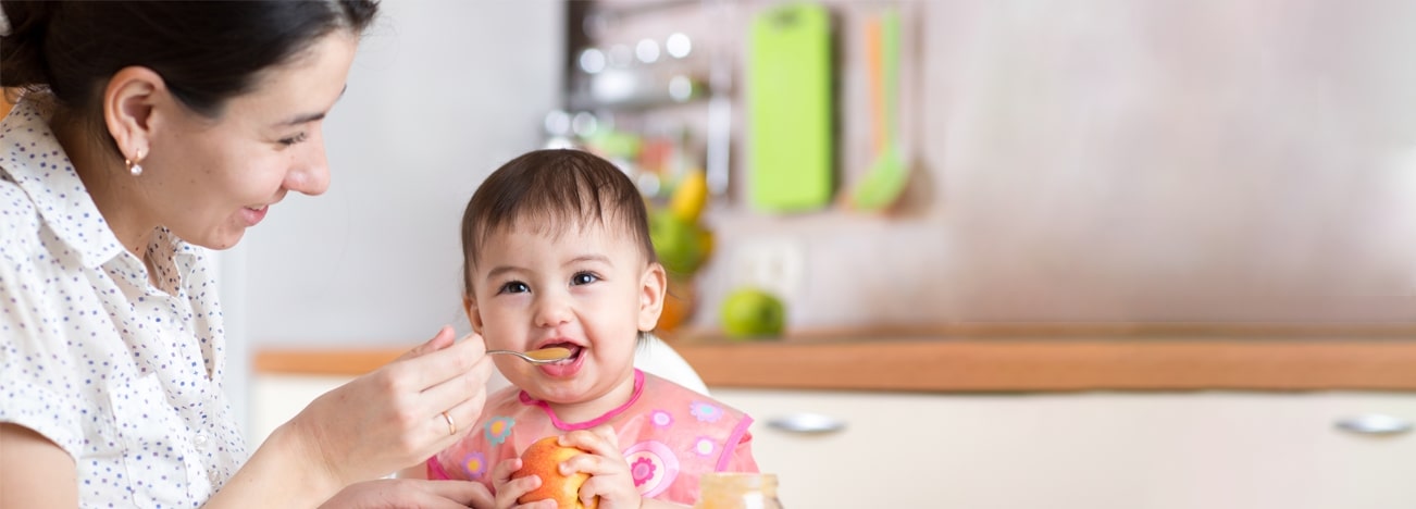 Mamá alimentando a su hijo con puré de frutas.