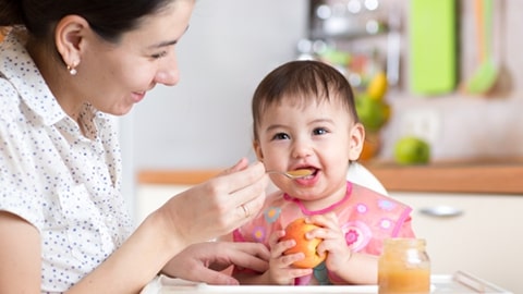 Mamá alimentando a su hijo con puré de frutas.