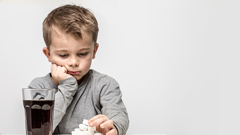 Niño pensativo sosteniendo fruta, con un vaso de refresco del otro lado.