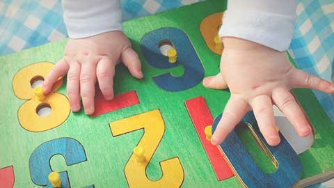 Manos de bebé en el suelo mientras toca textura de números y letras.